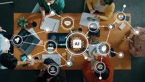 Overhead view of a diverse team around a wooden table, collaborating with laptops, charts, and AI holographic graphics projected above the workspace.